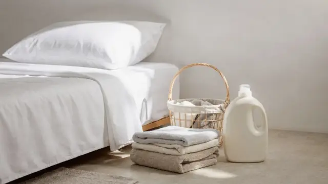 Kissenbezug auf dem Bett mit Wäschekorb und Weichspüler-Flasche zum Thema Weichspüler bei Kissenbezügen